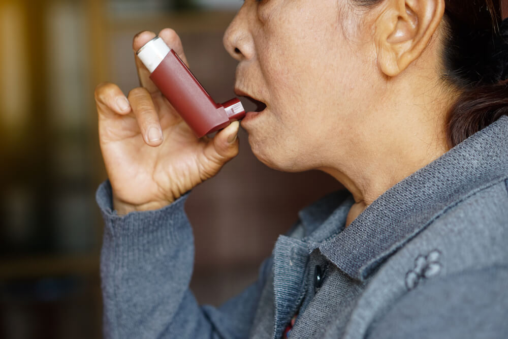 An asian woman or assigned-female-at-birth person is using an inhaler (for asthma)